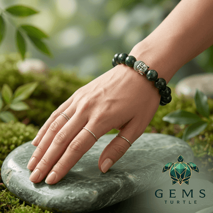 Hand wearing a green jade prosperity energy bracelet on a stone, surrounded by lush greenery, symbolizing abundance and harmony.